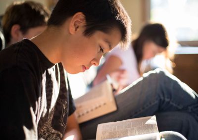 A little boy reading scriptures sitting next to other children reading